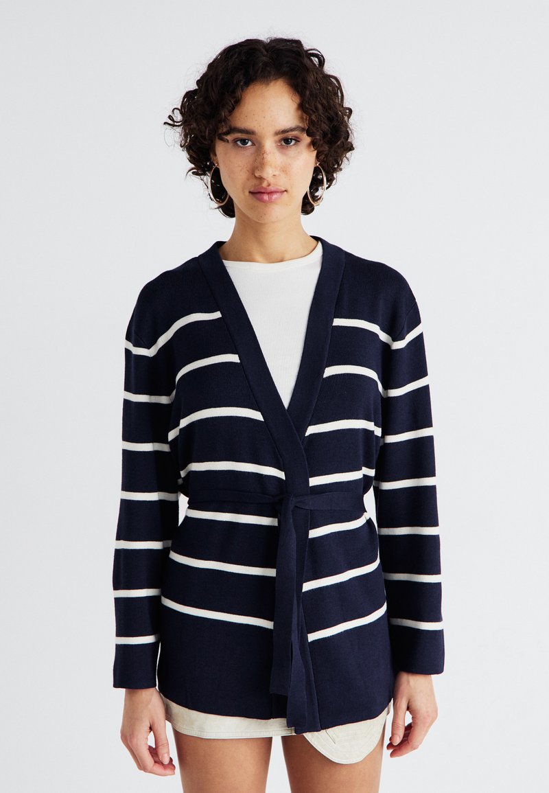Cardigã listrado azul-marinho com linhas brancas, design envolvente, mangas longas e um cinto amarrado na cintura. Material de malha macia com um ajuste descontraído.