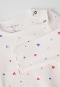 Witte geribbelde langarmtop met kleine roze, paarse en blauwe hartpatronen; heeft drukknoopjes bij de halslijn en een zachte textuur.