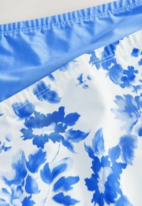 Ţesătură cu un model floral albastru, cu o textură netedă, având un brâu solid albastru şi un elastic strâns. Fundalul este alb.