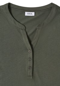 Chemise Henley vert olive avec trois boutons noirs et un col rond, arborant une étiquette de marque "CECIL" à l'intérieur du col.