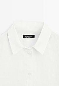 Camicia di lino bianca con collo classico e chiusura anteriore con bottoni, etichettata "Massimo Dutti", realizzata in un tessuto morbido e testurizzato.