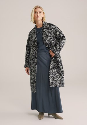 Abrigo de estampado de leopardo en gris y negro, con cuello muesca y abertura frontal, llevado sobre una blusa azul oscura y una falda gris, con tacones taupe.