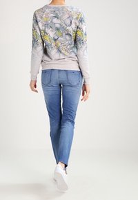 Felpa grigia chiara con un motivo floreale colorato sul retro, abbinata a jeans skinny di lavaggio medio e sneakers bianche.