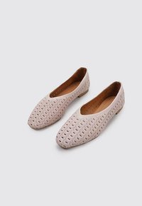 Zapatos planos de color rosa claro con un patrón de hojas perforado, punta redondeada y un tacón bajo y sólido. El interior tiene un forro suave en color tostado.