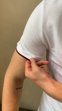 Kratki majica s kraticama bele boje iz teksturiranega materiala; ima črno-rdeč poudarek ob robu rokava; jo nosi roka, ki prilagaja manšeto.