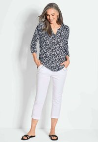 Blouse met bloemenpatroon in marineblauw, met ellebooglange mouwen en V-hals, gecombineerd met knielange witte broeken, aangevuld met zwarte sandalen.