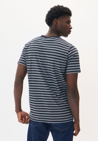 Jūrų ir šviesiai pilkos spalvos juostelėmis marškinėliai, trumpomis rankovėmis, apvaliu iškirpimu, pagaminti iš minkštos medžiagos, rodomi iš nugaros. Matosi džinsai.