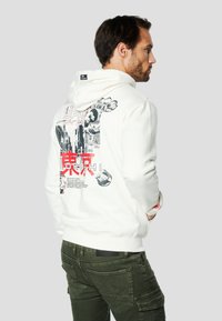 Biała bluza z kapturem z nadrukami graficznymi, w tym japońskim tekstem i obrazkami na plecach. Model z kapturem na sznurek i ściągaczami na mankietach.
