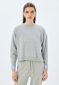 Sudadera gris con mangas largas, puños acanalados y un dobladillo corto, con acentos de rayas azules en los puños. Hecha de una tela suave.