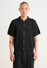 Black short-sleeve knitted cardigan with a collar, featuring a textured open pattern and brown buttons down the front.