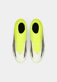 Ζευγάρι αθλητικών παπουτσιών σε νέον κίτρινο και λευκό, με μαύρες και κόκκινες λεπτομέρειες, από πάνω, σε λευκό φόντο.