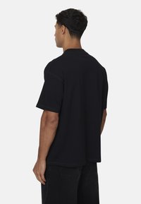 Czarny oversize t-shirt z krótkimi rękawami, okrągłym dekoltem i prostym wykończeniem. Tkanina wydaje się gładka, a krój jest luźny.