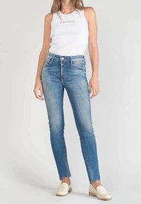 Jeans skinny in denim blu chiaro con effetto sbiadito, design a cinque tasche e accessori in metallo argento. Abbinati a una canotta bianca a coste.