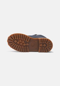 Suola in gomma con profondi tasselli, colore marrone. La parte superiore è di un blu scuro con una cerniera laterale e il logo Timberland vicino al tallone.