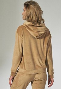 Brązowa bluza z kapturem wykonana z miękkiego materiału, o luźnym kroju, z prążkowanymi mankietami i gładką fakturą, przedstawiona z tyłu.
