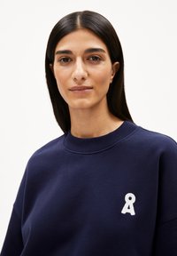 Navy sweatshirt featuring a crew neck and a white embroidered logo on the chest. Smooth texture with a relaxed fit.