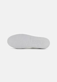 Weiße Gummisohle des Sneakers mit einem gerippten Muster und erhobenem Logo. Glatte Textur mit Eindrückmarkierungen und Größenprägung.