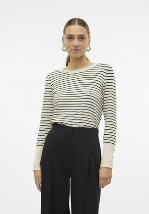 Maglietta a maniche lunghe a righe color crema con righe nere, con bottoni decorativi sui polsini, abbinata a pantaloni neri a vita alta.