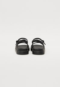 Zwarte sandalen met een platte zool, dubbele banden en een verstelbare enkelband. Gladde afwerking met een minimalistisch design.