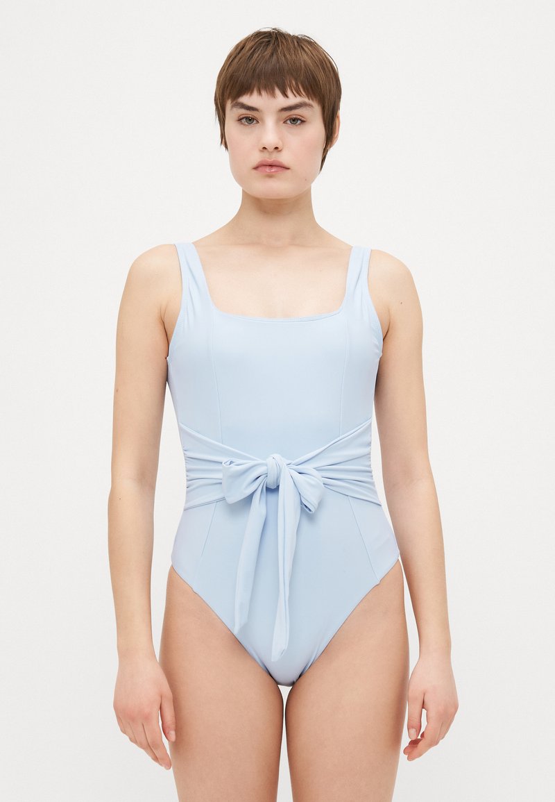 Fato de banho azul claro em uma peça só, com decote quadrado, alças largas e detalhe de atilho à frente na cintura. Tecido liso e elástico.