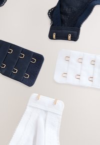 Allonges de soutien-gorge noir et blanc et bretelles en dentelle assorties avec des crochets dorés sur un fond neutre.