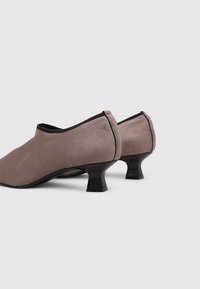 Zapatos de ante gris con un tacón negro bajo y curvado. Textura suave con detalles de costura mínimos y un diseño de puntera redondeada.