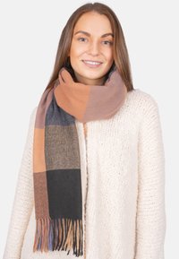 Étole tissée en marron, gris et rouille avec un motif à carreaux et des bords à franges, portée sur un pull en tricot léger texturé.
