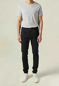 Jeans negros y una camiseta gris claro combinados con zapatillas blancas. Los jeans tienen una silueta ajustada y una textura suave.