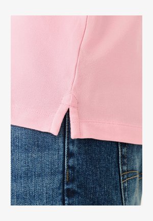 Rozā polo krekls ar teksturētu audumu, ar sānu spraugām un taisnu apakšējo malu, apvienots ar ziliem džinsiem.