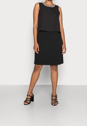 Czarny bezrękawnik z zaokrąglonym dekoltem i ozdobnym obszyciem, zestawiony z czarną dopasowaną spódnicą do kolan oraz czarnymi sandałami na wysokim obcasie z paskami.