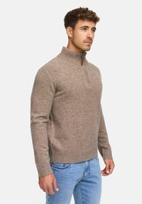 Brun zip-neck tröja i mjukt texturerat stickat material, med ribbad krage och manschetter, kombinerad med ljusblå denimjeans.