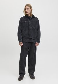 Sort denimjakke med krave, frontlommer og knaplukning, parret med løstsiddende sorte bukser. Glat tekstur, minimalistisk design.
