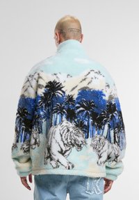 Faux fur pullover with a mountain and palm tree pattern in blue and white, featuring tigers on a light blue background. High collar and loose fit.