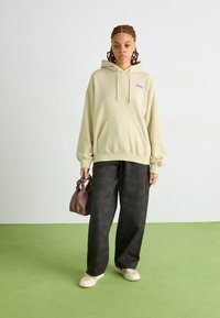 Moletom bege claro com o texto 'obey', calças largas cinza com padrão e uma pequena bolsa rosa. Os sapatos são de cor clara e simples.