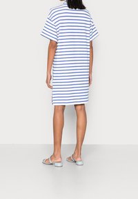 Pasiasta sukienka w białym i niebieskim kolorze, krótki rękaw, do kolan, z bocznymi rozcięciami. W połączeniu z jasnoniebieskimi klapkami.