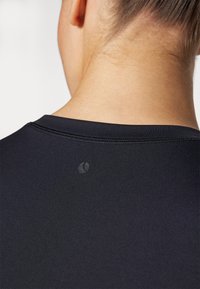 Camisola atlética preta com uma textura suave, decote arredondado e um pequeno detalhe com o logótipo perto do colarinho nas costas.