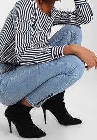 Striped long-sleeve top in navy and white, light blue skinny jeans with zipper detail, and black pointed stiletto ankle boots.