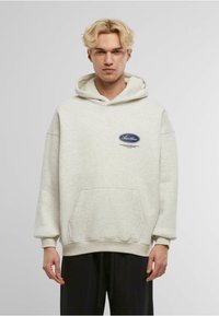 Hoodie grigio chiaro realizzato in misto cotone, con tasca a marsupio frontale, cappuccio con cordini e patch con logo sul petto. Vestibilità rilassata.