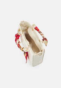 Cream-colored handbag with a textured pattern, gold hardware, and two fabric handles featuring red and patterned accents.