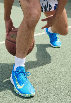 Personne portant des baskets bleu vif en train de dribbler un ballon de basket sur un terrain extérieur avec une surface verte visible et des lignes blanches.