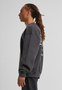 Grå sweatshirt med en afslappet pasform, der har sænkede skuldre og ribbede manchetter. Synlig broderi og en blød tekstur. Styles med mørke jeans.