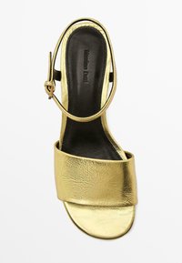 Sandale à talons hauts en métal doré avec une large tige avant et une fine lanière à la cheville, dotée d'une semelle intérieure noire lisse et d'un design minimaliste.