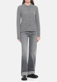 Cardigan grigio in maglia con bottoni, colletto e tasca frontale, abbinato a jeans a gamba larga grigio chiaro e stivali neri.