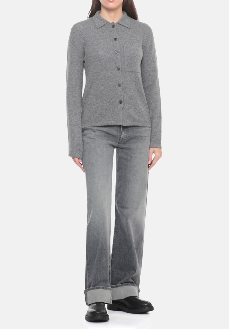 Cardigan grigio in maglia con bottoni, colletto e tasca frontale, abbinato a jeans a gamba larga grigio chiaro e stivali neri.