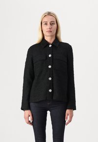 Jachetă neagră texturată cu guler, buzunare frontale și butoane decorative în formă de floare argintie. Mâneci lungi și croială lejeră.