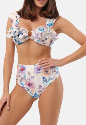 Donna che indossa un bikini floreale a vita alta con top arricciato con fiori viola, blu e arancioni su uno sfondo chiaro.