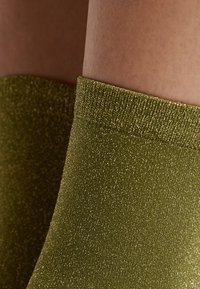 Calcetines tobilleros brillantes de color verde oliva con un borde acanalado. Tienen una superficie texturizada con hilos metálicos para un brillo sutil.