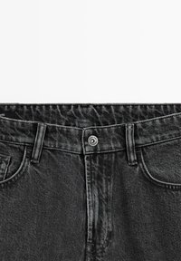 Close-up of black denim jeans waist with button, belt loops, and front pockets visible against a white background.