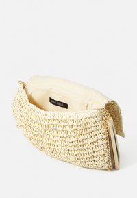 Pochette tissée de couleur crème avec un extérieur texturé, des accents en métal doré et une doublure en tissu. Contient une étiquette intérieure avec le nom "ANNA FIELD".