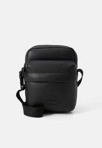 Musta, teksturoitu nahkalaukku, jossa on vetoketjusuljin, etupuolen logokilpi ja säädettävä hihna. Suorakaiteen muotoinen, kompakti muotoilu.